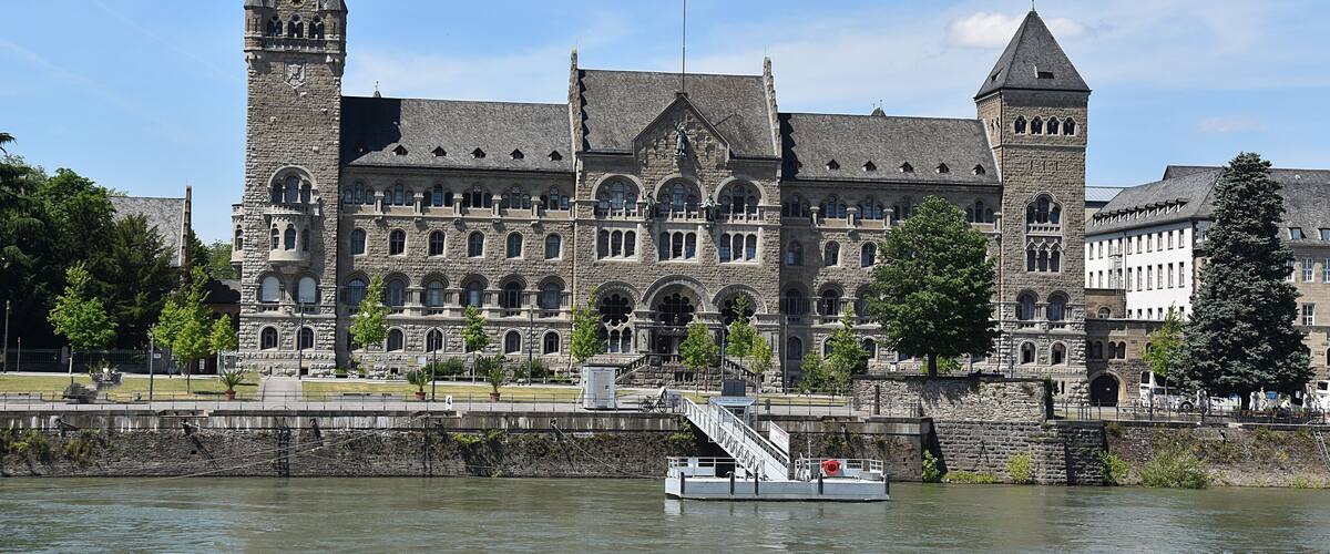 A historic stone building with two towers and a river in the foreground.