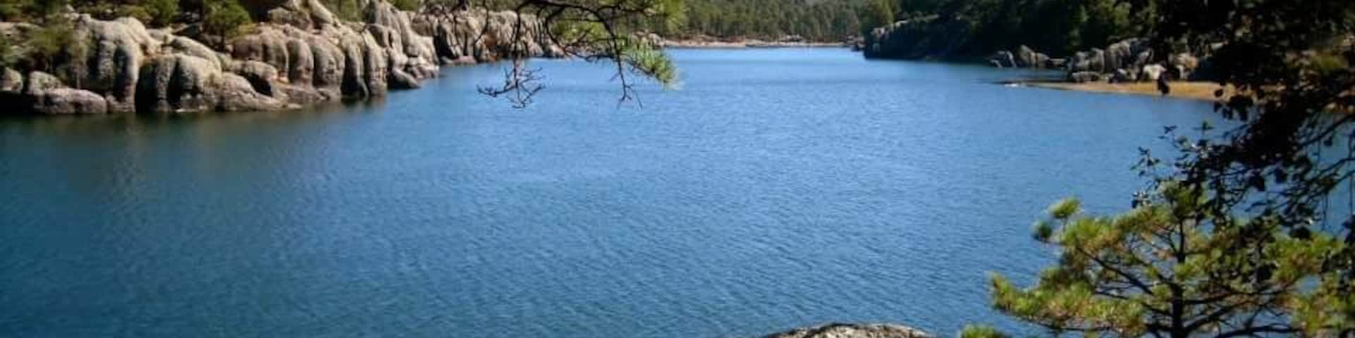 A calm lake surrounded by rocky terrain and sparse trees.