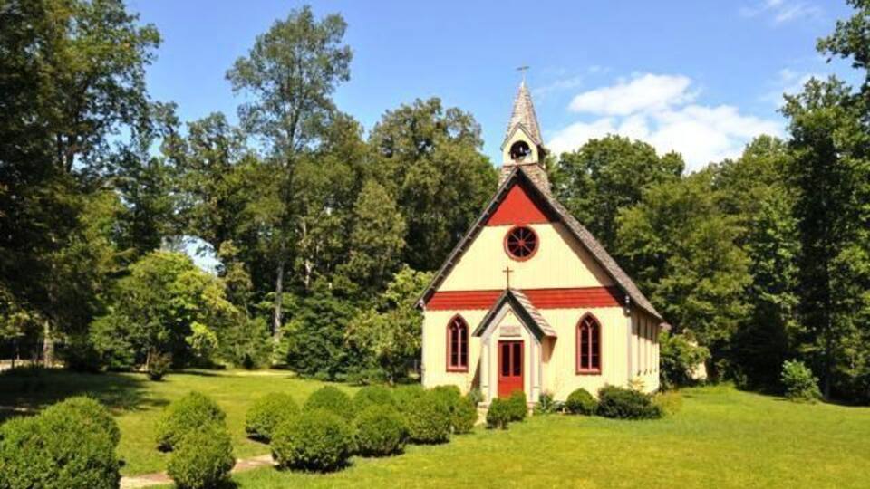 A small church with a red roof and white walls, surrounded by a well-maintained lawn and trees.