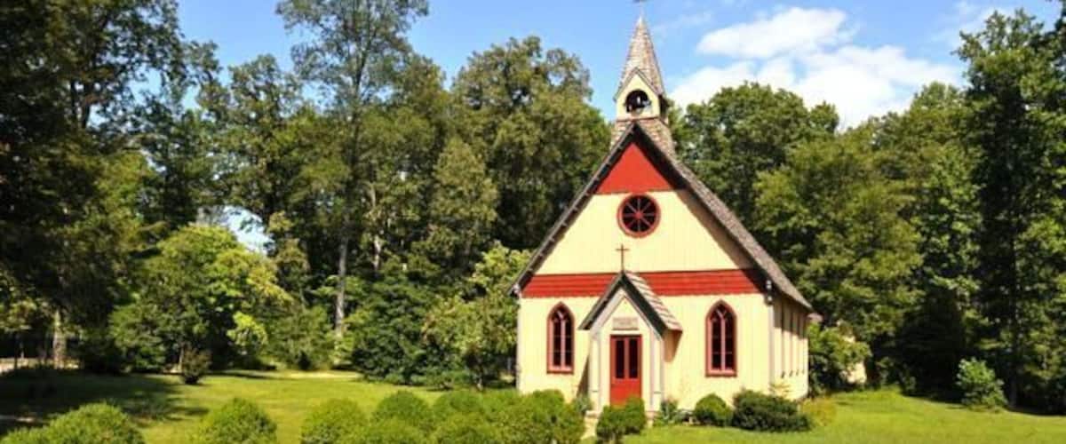 A small church with a red roof and white walls, surrounded by a well-maintained lawn and trees.