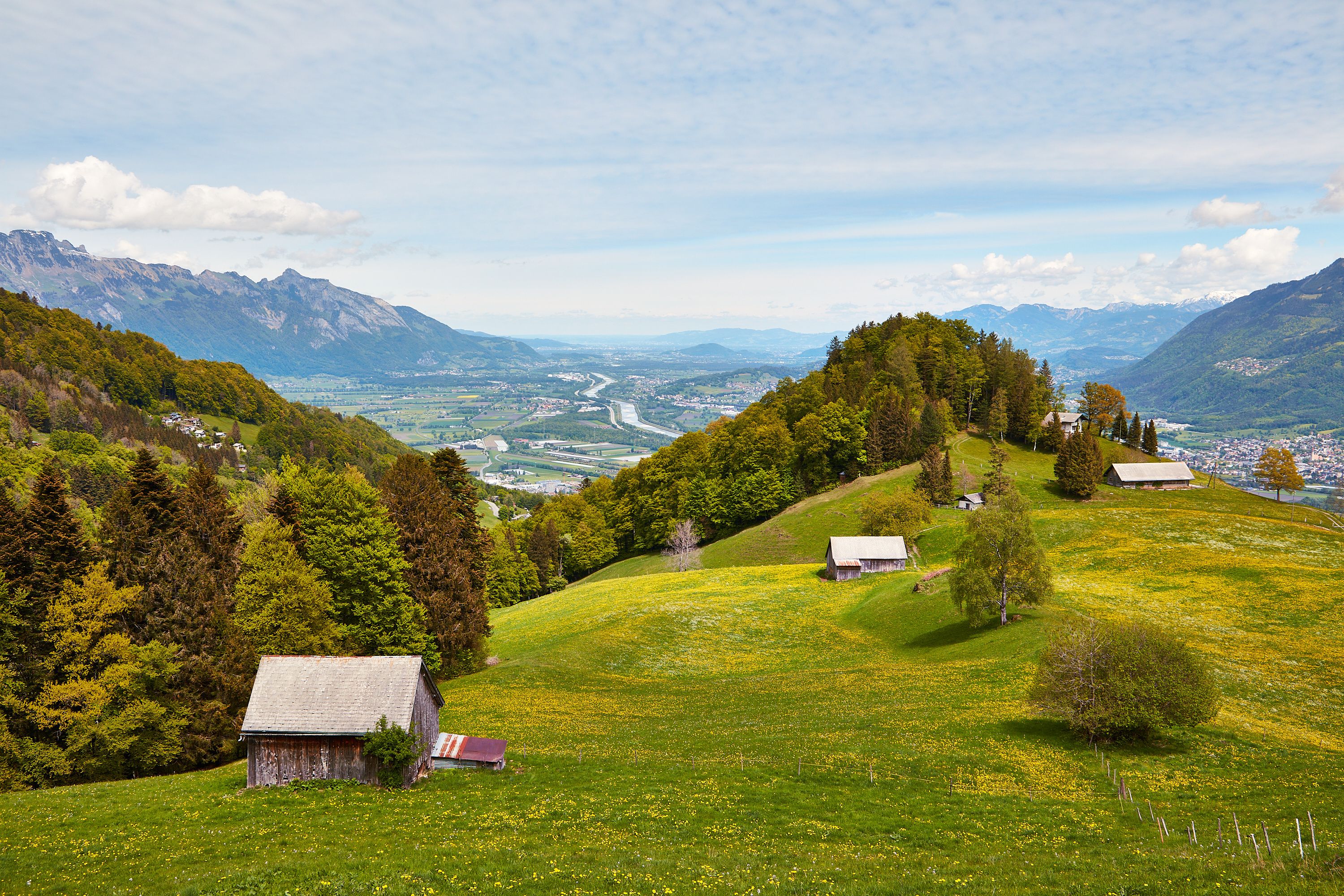 Paesaggio rurale con dolci colline, un fiume e montagne sullo sfondo.