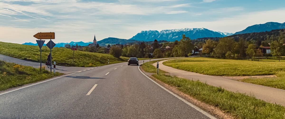 A road leading to a mountain range with a church and a sign for 'Schodling'.