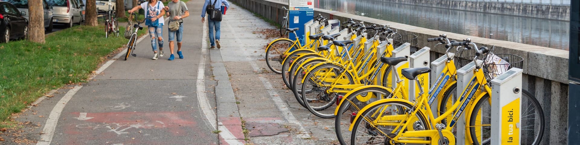 A bike rental station with yellow bikes, a river, and buildings in the background.