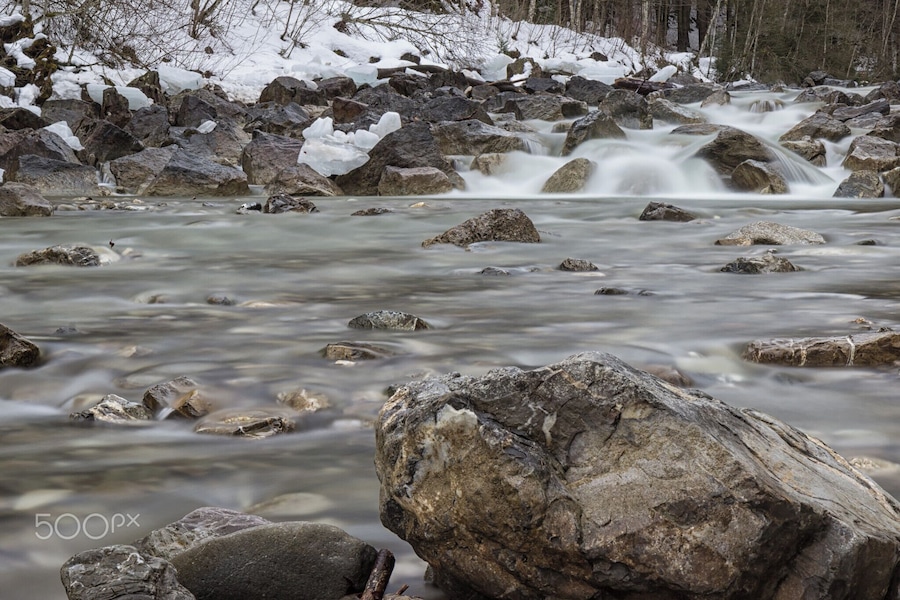Un río con cascada, rodeado de rocas y nieve.