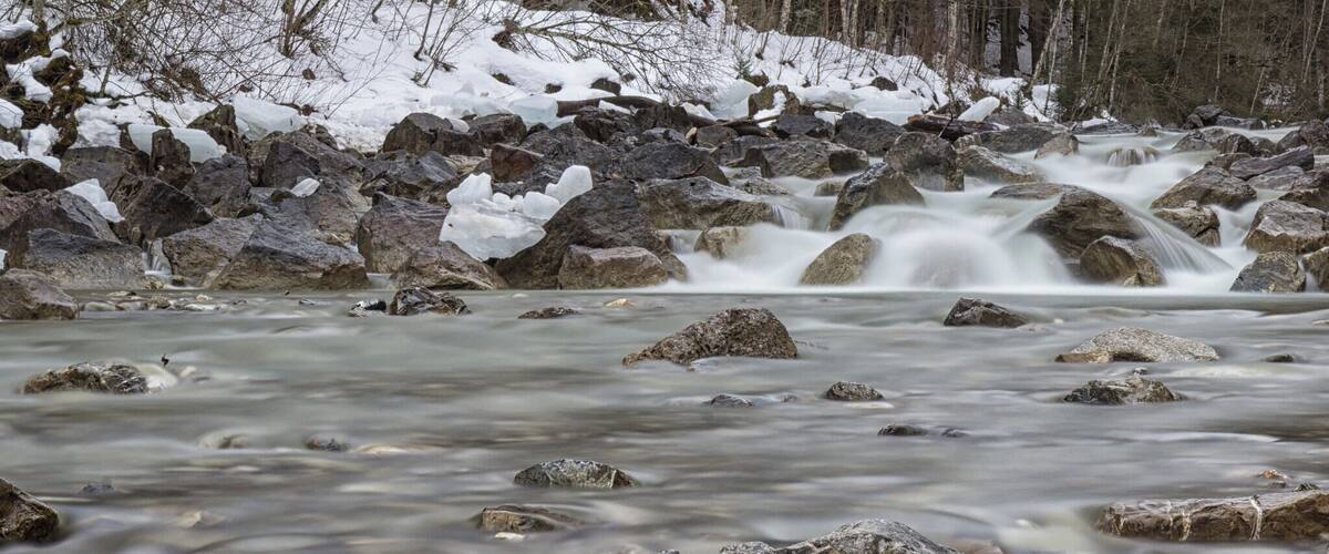 A river with a waterfall, surrounded by rocks and snow.