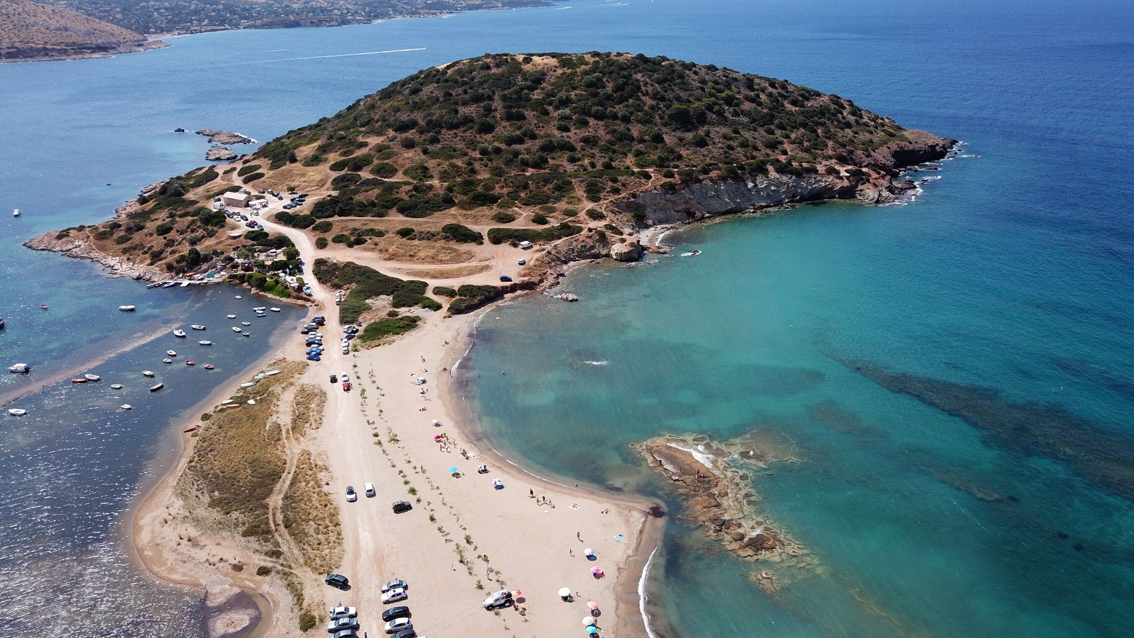 Vista aèria d'una zona costanera amb una platja de sorra, un petit turó amb vegetació escassa i embarcacions a l'aigua.