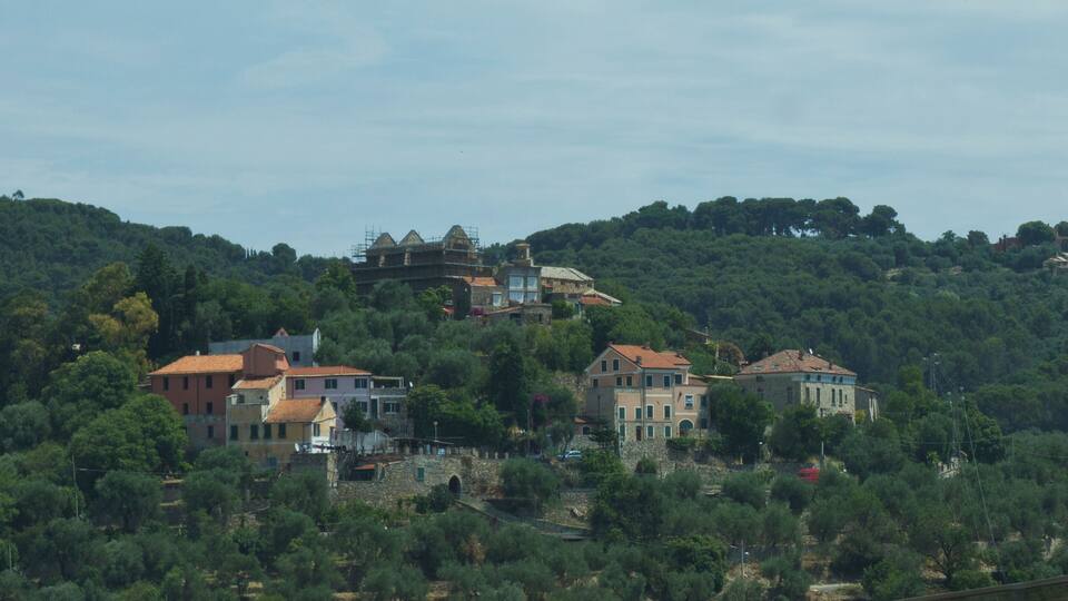 A hillside with several buildings, including a large house with a red roof and a smaller building with a pink roof.