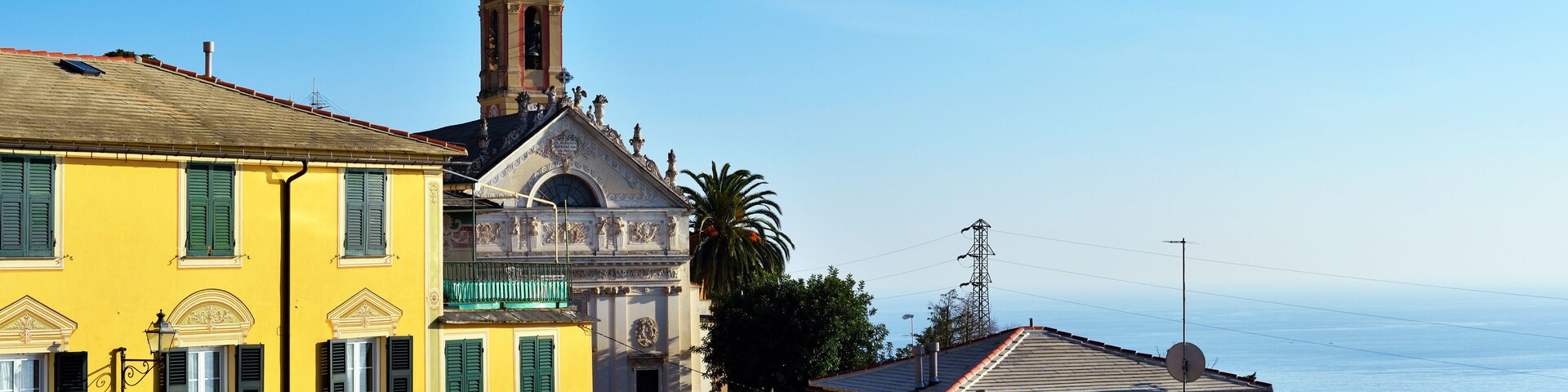 Un pueblo costero con una destacada torre de iglesia, edificios coloridos y una vista despejada del mar.