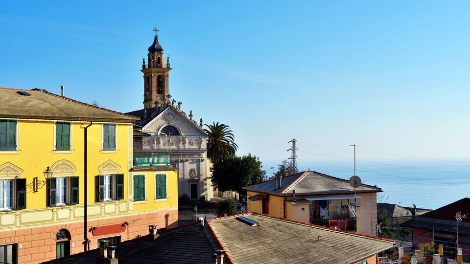 A coastal town with a prominent church tower, colorful buildings, and a clear view of the sea.