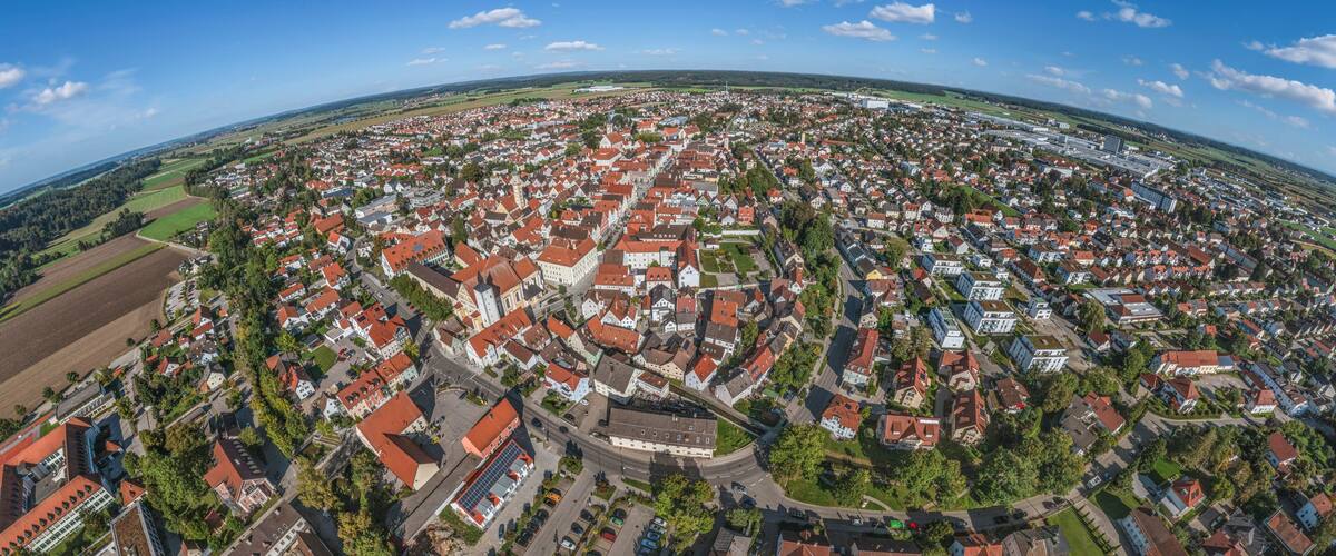 An aerial view of a town with red-roofed houses, a church, and surrounding fields.