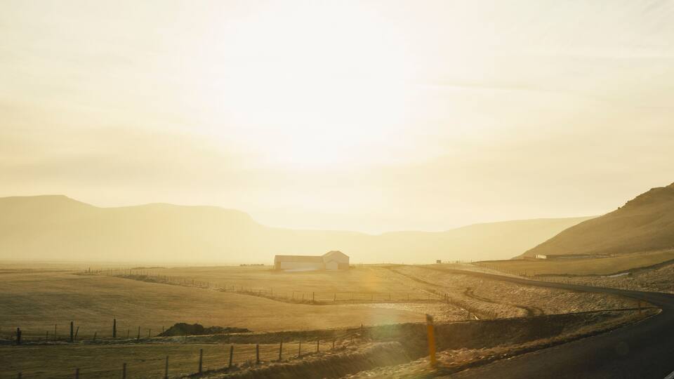 A rural landscape with a winding road, a barn, and rolling hills in the background.