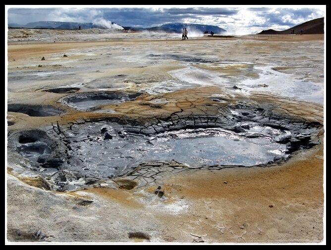 A geothermal area with bubbling mud pools and a person in the distance.