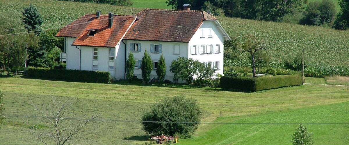 A white house with a red roof surrounded by lush green fields and trees.