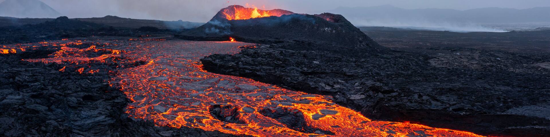 A volcanic landscape with flowing lava and a mountain in the background.