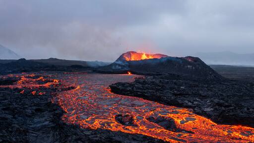 A volcanic landscape with flowing lava and a mountain in the background.