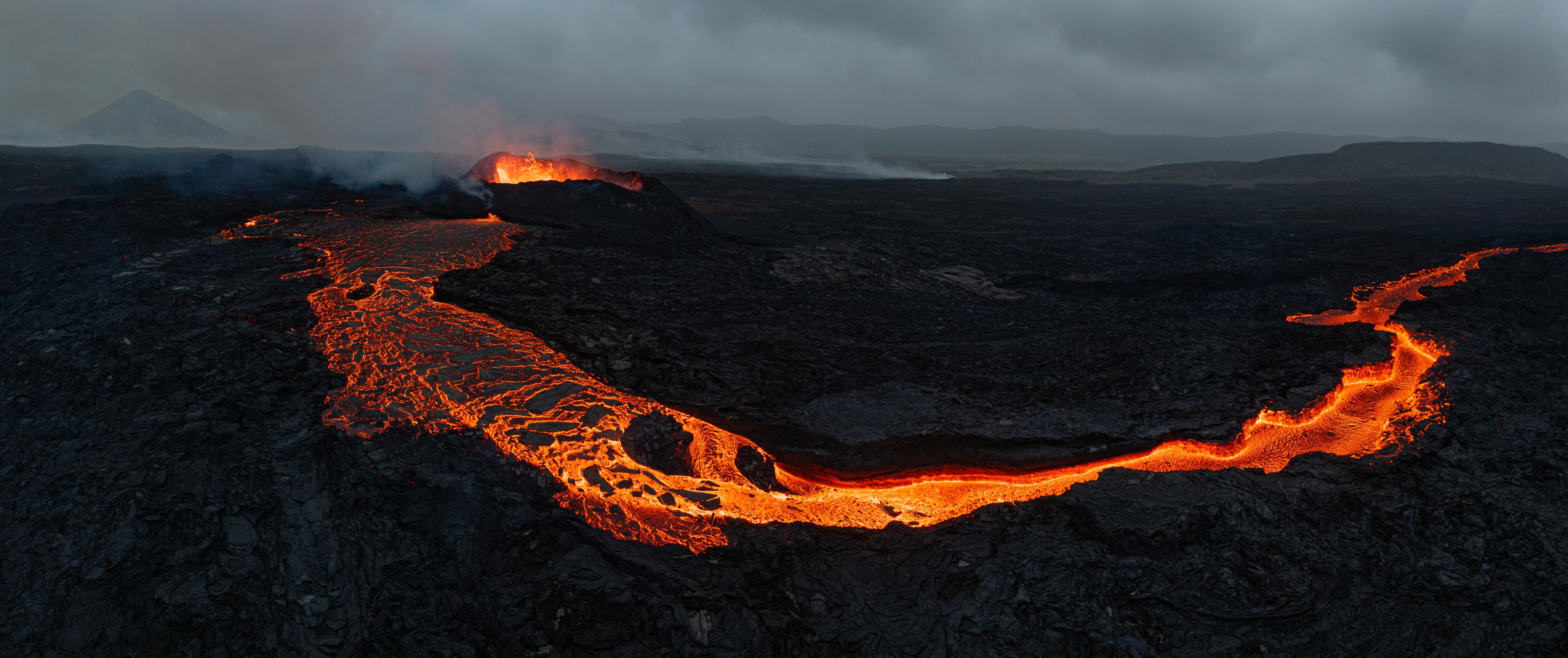 Ett vulkaniskt landskap med flytande lava och ett berg i bakgrunden.