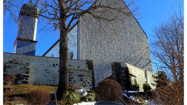 A building with a unique geometric facade, a tall tower, and a tree in the foreground.