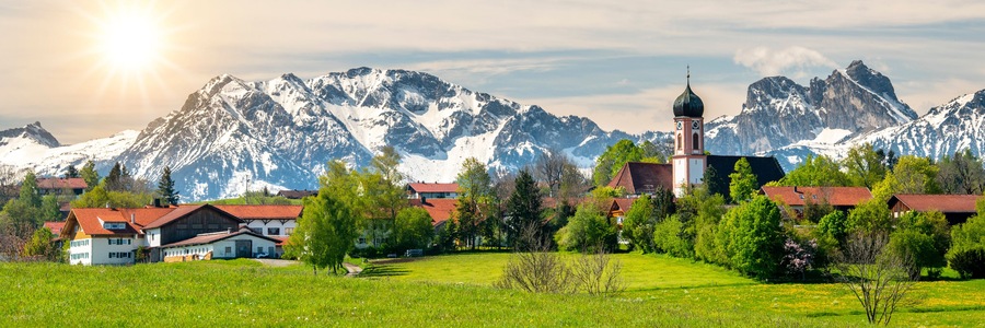 Un pueblo con una iglesia, rodeado de montañas nevadas y campos verdes.