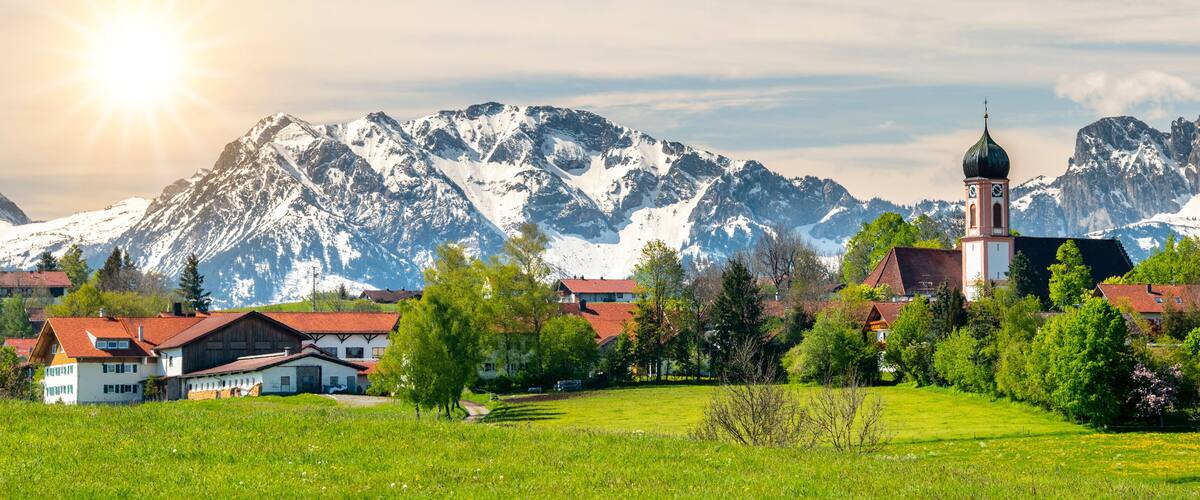 A village with a church, surrounded by snow-capped mountains and green fields.