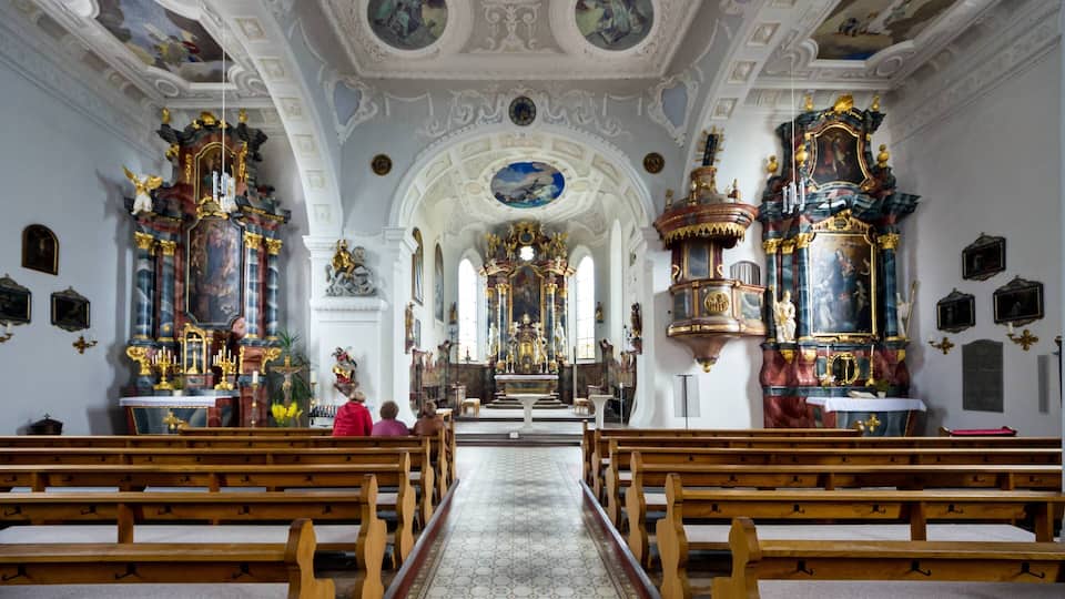 An ornate church interior with wooden pews, a central altar, and elaborate decorations.