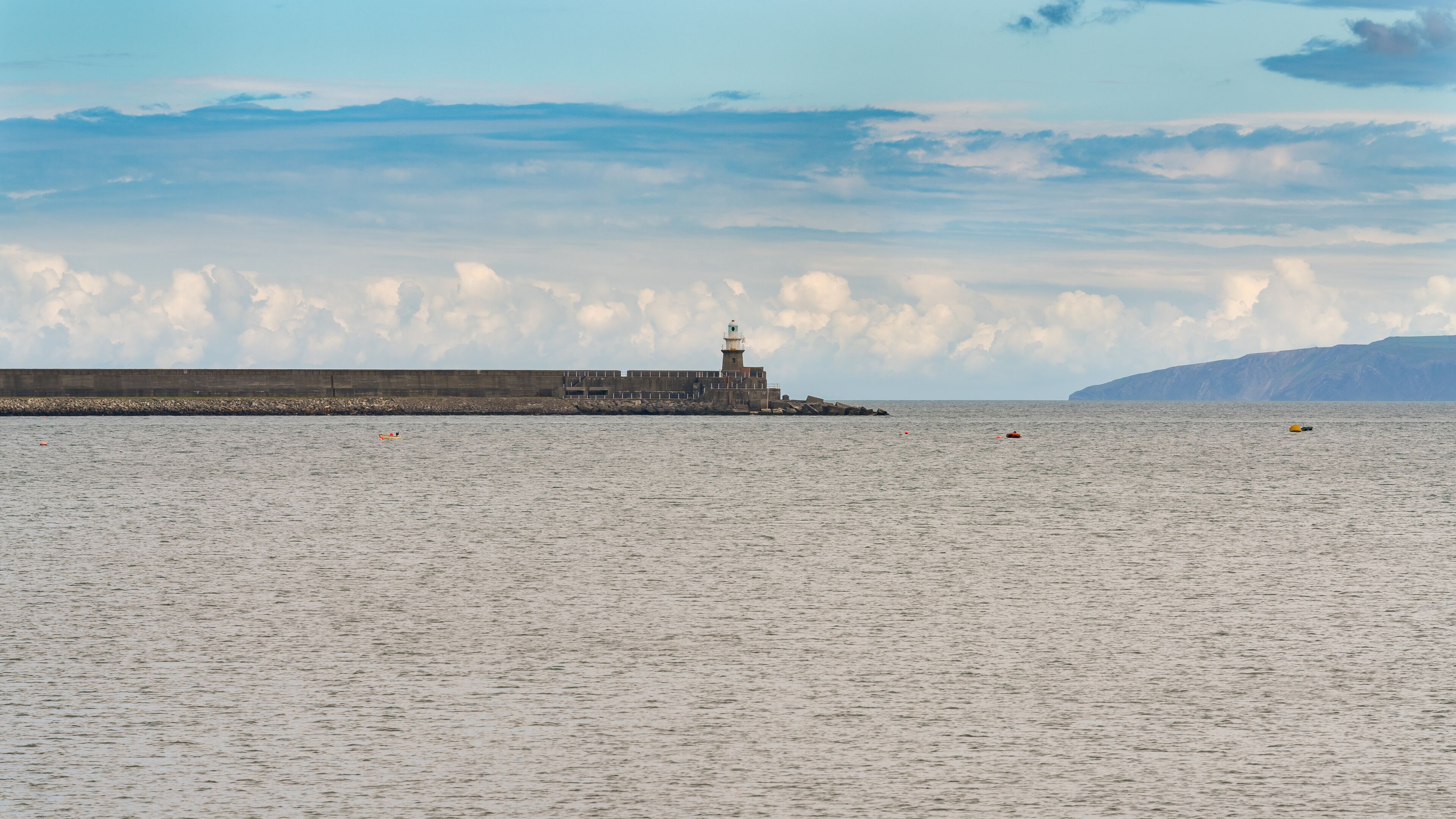 A lighthouse at a harbor with calm water and a cloudy sky.