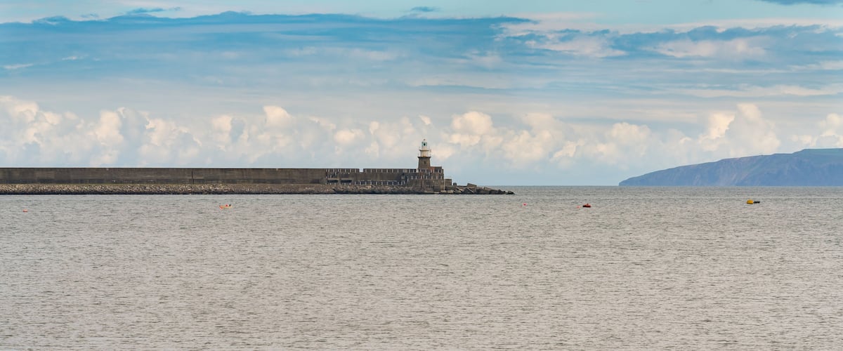 A lighthouse at a harbor with calm water and a cloudy sky.