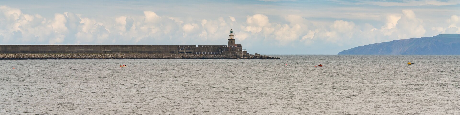 A lighthouse at a harbor with calm water and a cloudy sky.