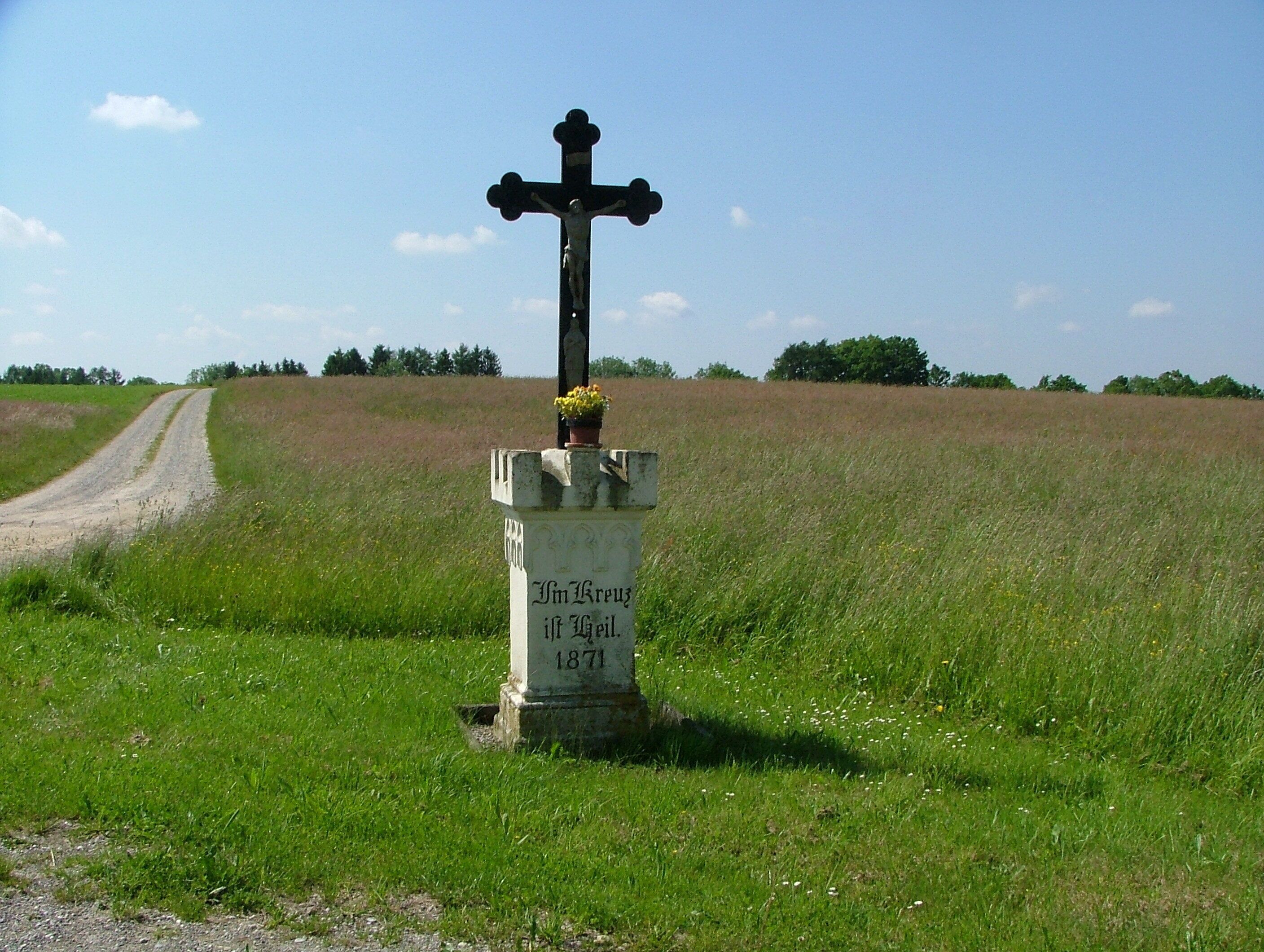 A rural cross with a gravestone in a field.