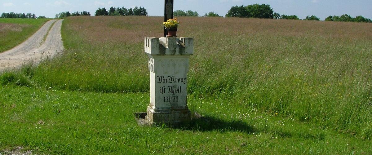 A rural cross with a gravestone in a field.