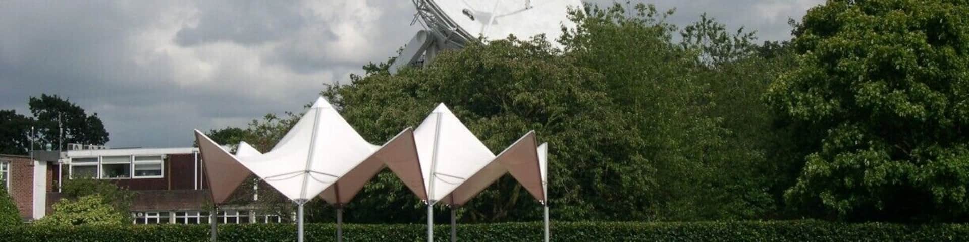 The Jodrell Bank Observatory (originally the Jodrell Bank Experimental Station, then the Nuffield Radio Astronomy Laboratories from 1966 to 1999; /ˈdʒɒdrəl/) is a British observatory that hosts a number of radio telescopes, and is part of the Jodrell Bank Centre for Astrophysics at the University of Manchester. The observatory was established in 1945 by Sir Bernard Lovell, a radio astronomer at the University of Manchester who wanted to investigate cosmic rays after his work on radar during the Second World War. It has since played an important role in the research of meteors, quasars, pulsars, masers and gravitational lenses, and was heavily involved with the tracking of space probes at the start of the Space Age. The managing director of the observatory is Professor Simon Garrington.
The main telescope at the observatory is the Lovell Telescope, which is the third largest steerable radio telescope in the world. There are three other active telescopes located at the observatory; the Mark II, as well as 42 ft (13 m) and 7 m diameter radio telescopes. Jodrell Bank Observatory is also the base of the Multi-Element Radio Linked Interferometer Network (MERLIN), a National Facility run by the University of Manchester on behalf of the Science and Technology Facilities Council.
The site of the observatory, which includes the Jodrell Bank Visitor Centre and an arboretum, is located in the civil parish of Lower Withington (the rest being in Goostrey civil parish), near Goostrey and Holmes Chapel, Cheshire, North West England. It is reached from the A535. An excellent view of the telescope can be seen by travelling by train, as the main line between Manchester and Crewe passes right by the site, with Goostrey station being only a short distance away.