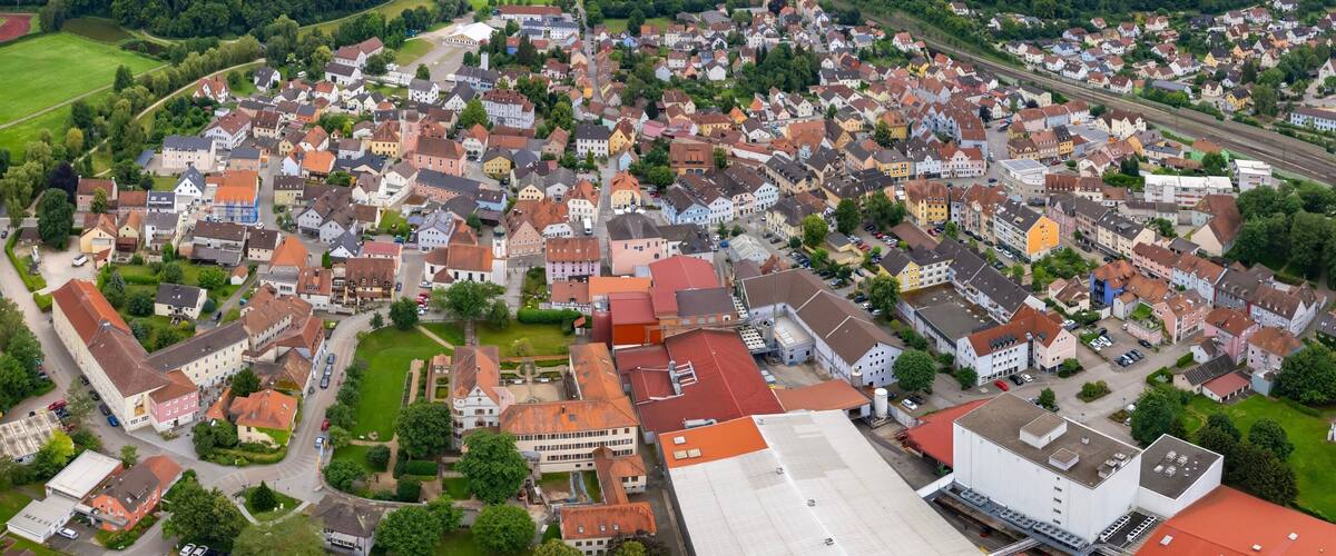 An aerial view of a densely populated town with a mix of residential houses, a railway line, and a large industrial building.