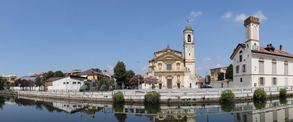 A historic town with a prominent church, a bell tower, and a canal reflecting the architecture.