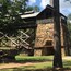 A stone building with a wooden structure on top, surrounded by trees and grass.