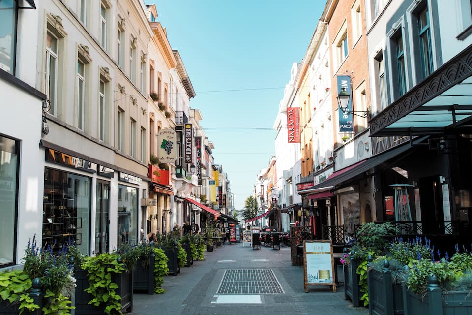 A narrow street lined with shops and cafes, with planters and outdoor seating.