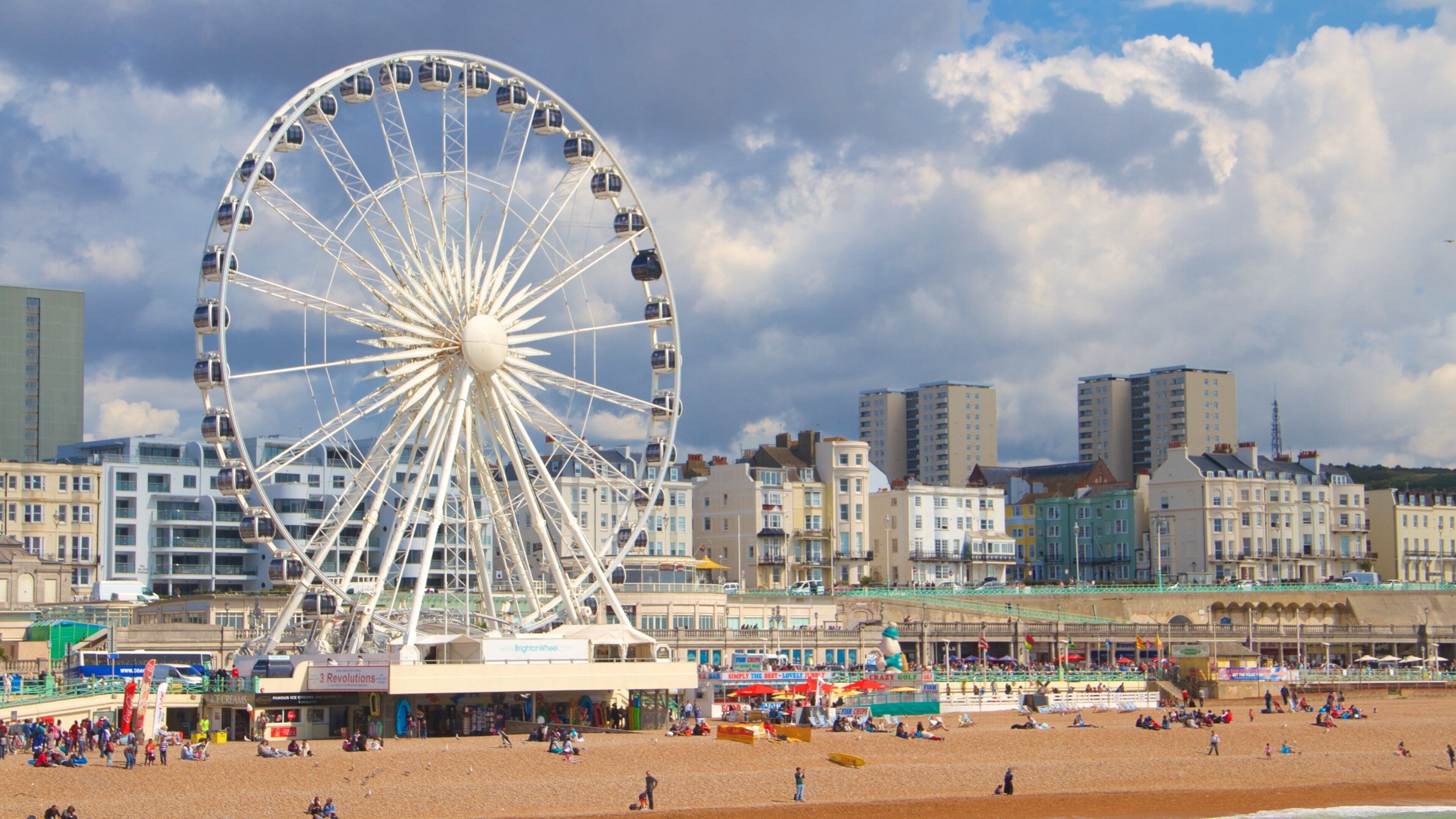 Uma roda gigante, uma praia e um horizonte urbano com edifícios.
