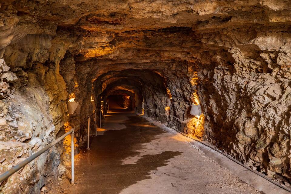 A tunnel with rough rock walls and a metal railing.