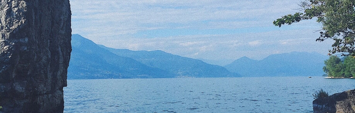 A rocky shoreline with clear water, a large rock formation, and distant mountains.