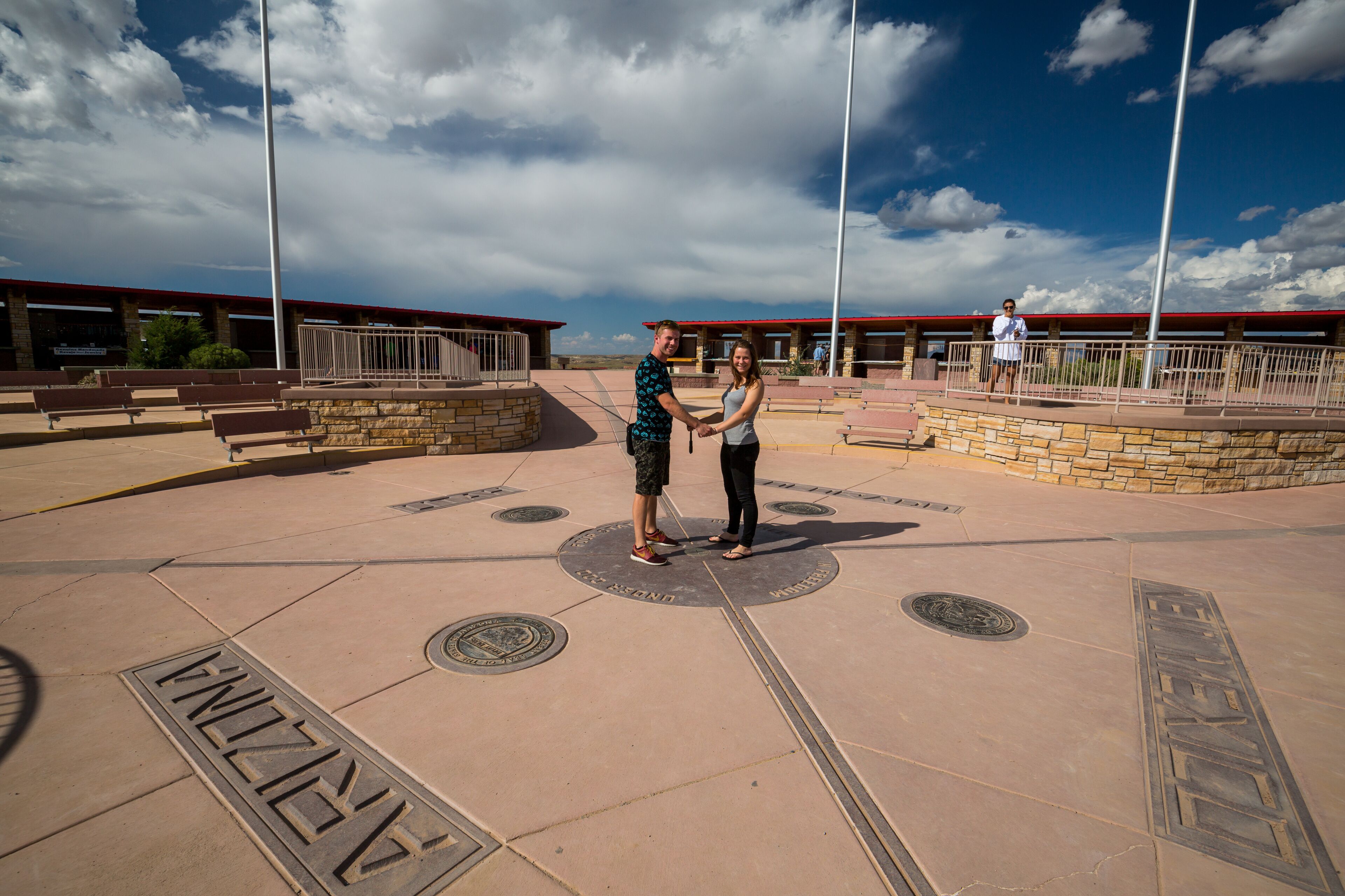 Two people holding hands in a plaza with a stone wall and benches.