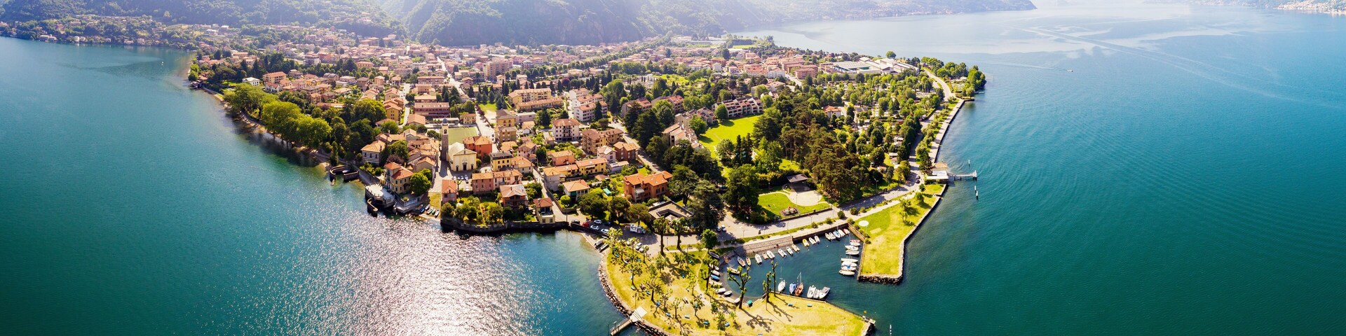 An aerial view of a lakeside town with a marina, surrounded by mountains and lush greenery.