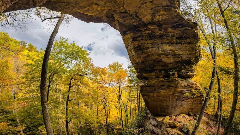 Une arche naturelle formée par la roche, entourée d’arbres aux couleurs automnales.