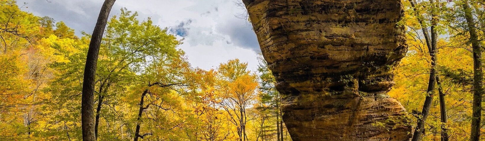 Formação rochosa natural em arco, rodeada por árvores com folhagem avermelhada do outono.