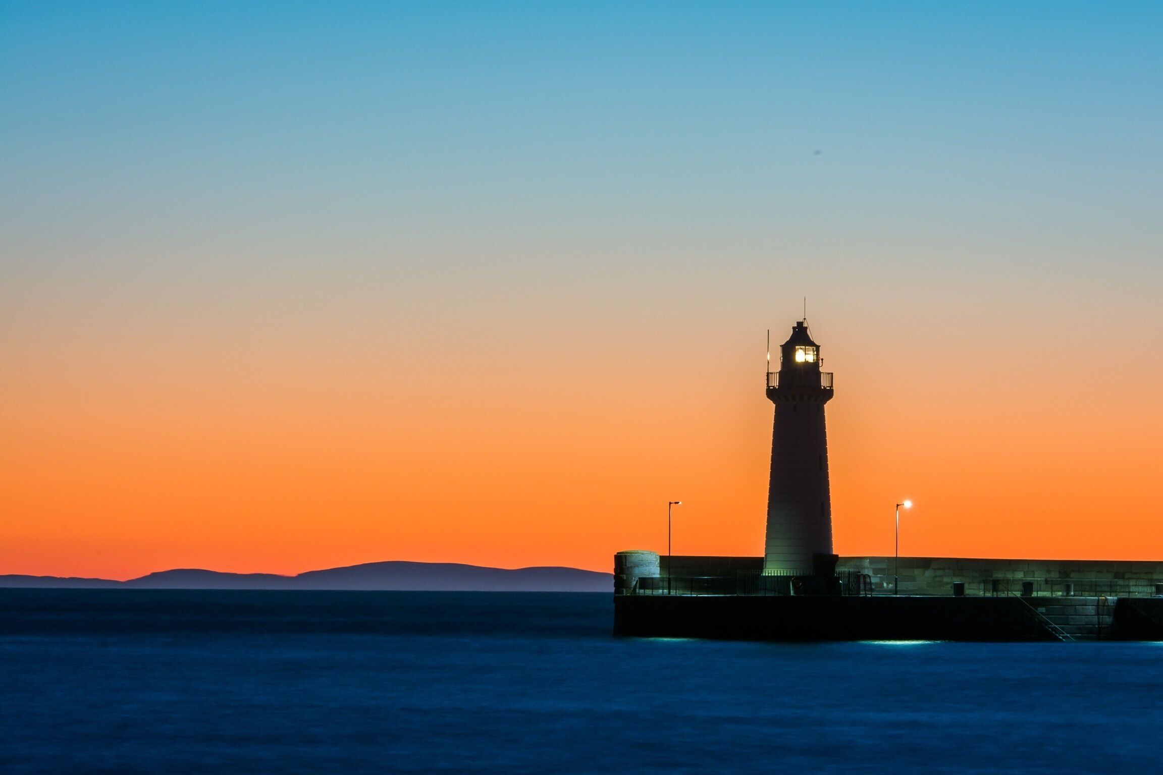 A lighthouse at sunset with a clear sky and calm sea.