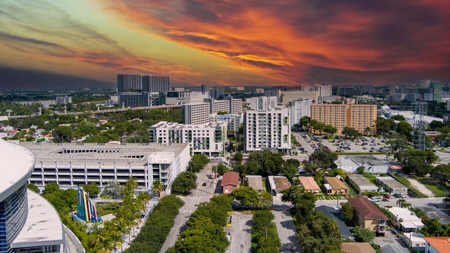 stunning aerial view with hotels, office buildings, apartments and homes in the city skyline and parking lots and LoanDepot Park surrounded by lush green trees at sunset in Miami Florida