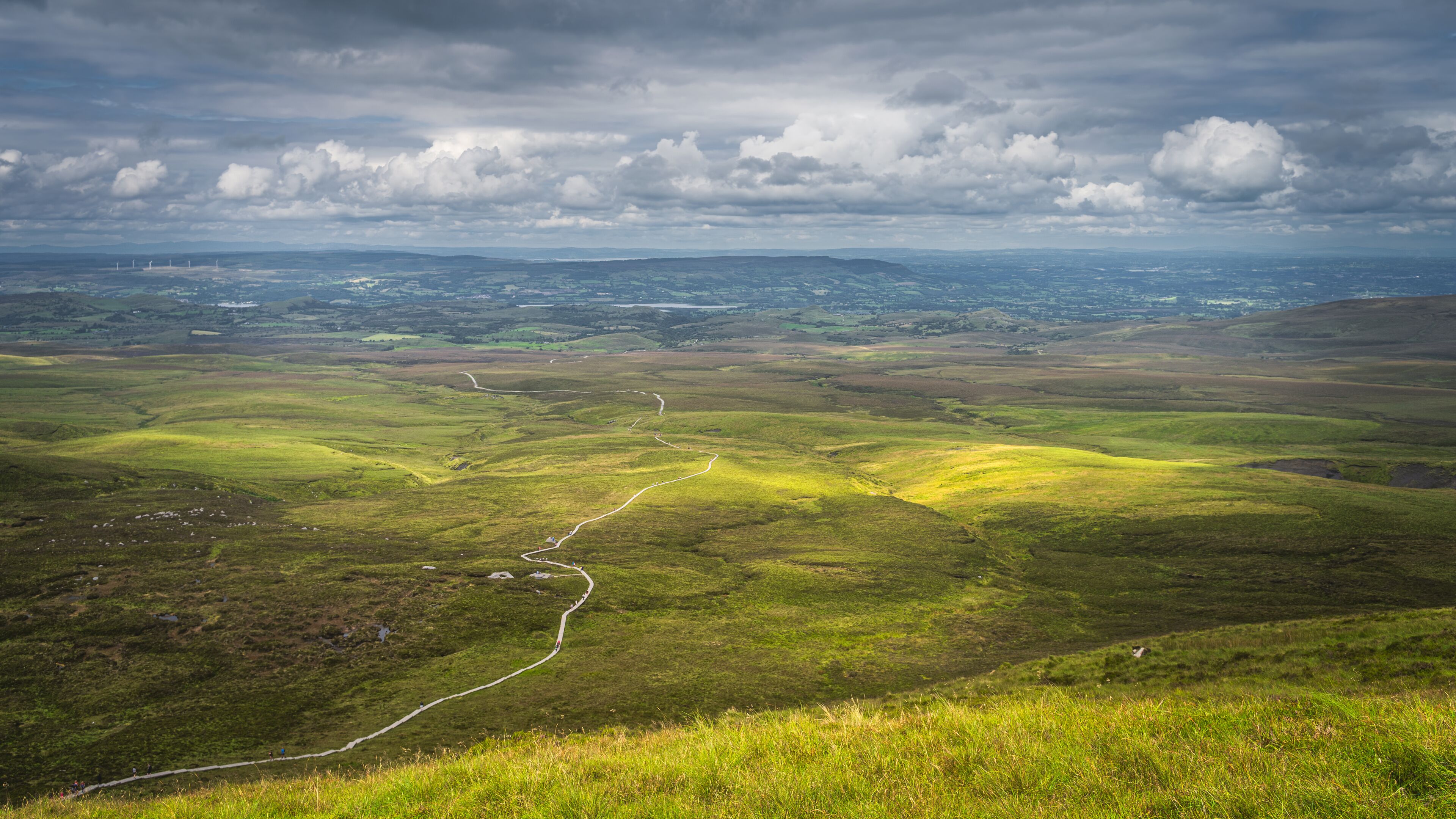 A vast green landscape with rolling hills and a winding road.