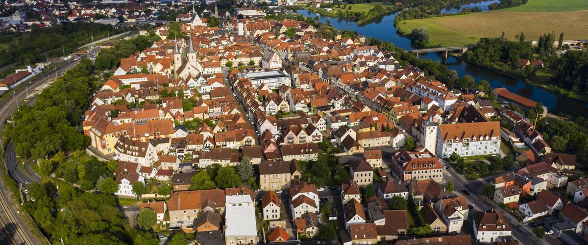 An aerial view of a historic town with a river, surrounded by greenery and featuring a prominent church and castle.