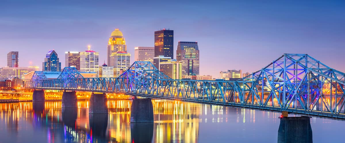 A city skyline with illuminated buildings and a blue-lit bridge over a calm body of water.
