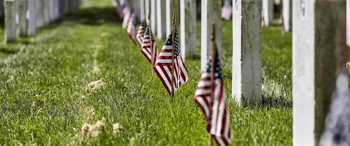 A cemetery with rows of white headstones and American flags planted in the grass.