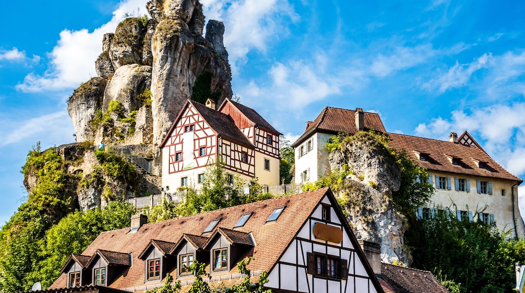 A mountain village with traditional half-timbered houses, a prominent rocky peak, and a clear blue sky.