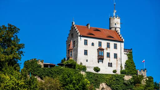 A castle with a red-tiled roof, white walls, and a tower with a flag.