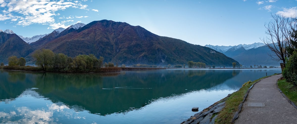 A calm lake with mountains in the background and a path along the shore.